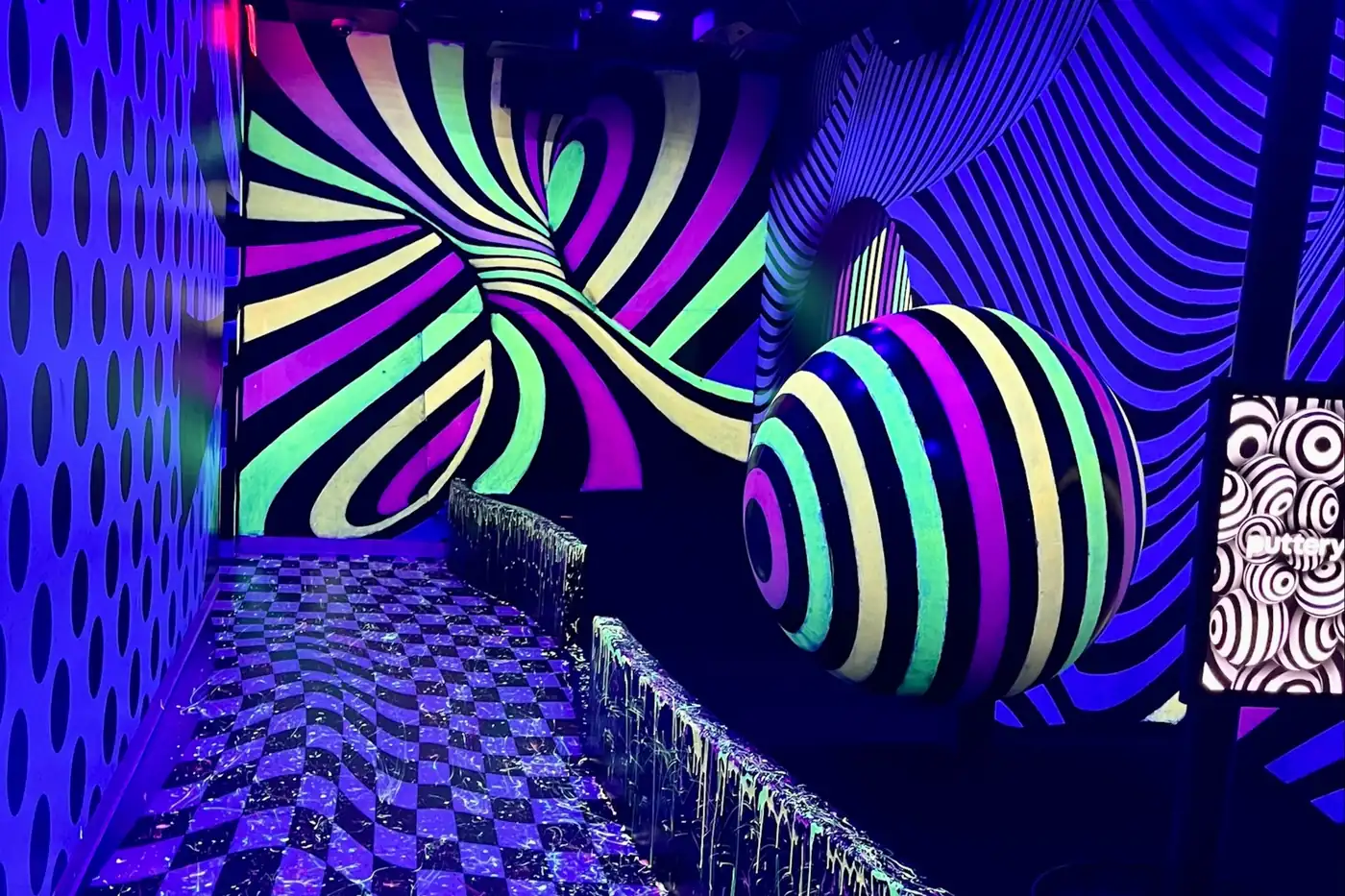 Glow-in-the-dark optical illusion mini golf hole with swirling neon patterns and a striped spherical feature inside the Illusion course at Puttery Dallas.