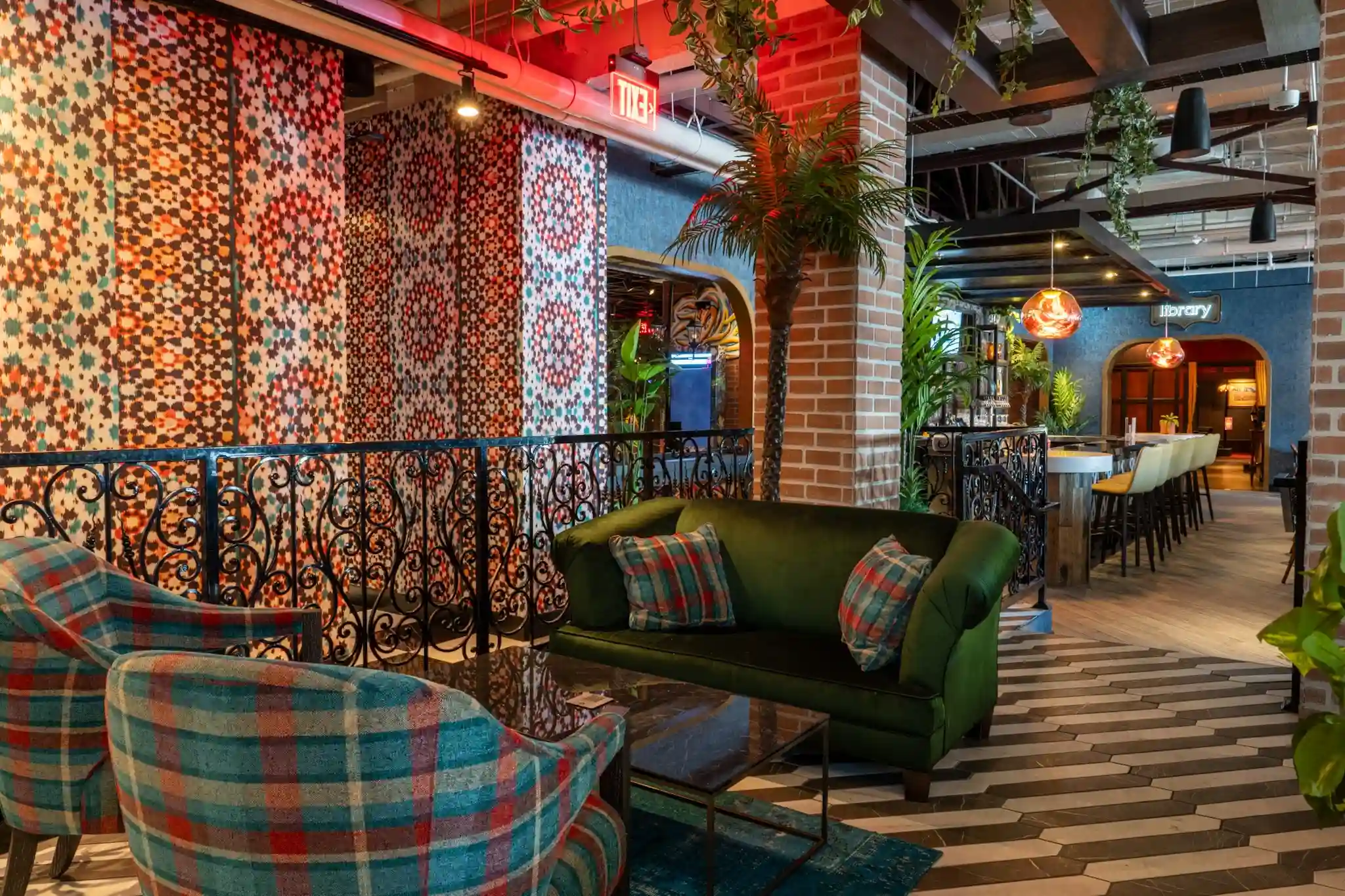 Lounge seating at Puttery Miami with a green sofa, plaid armchairs, tropical plants and bold patterned walls.