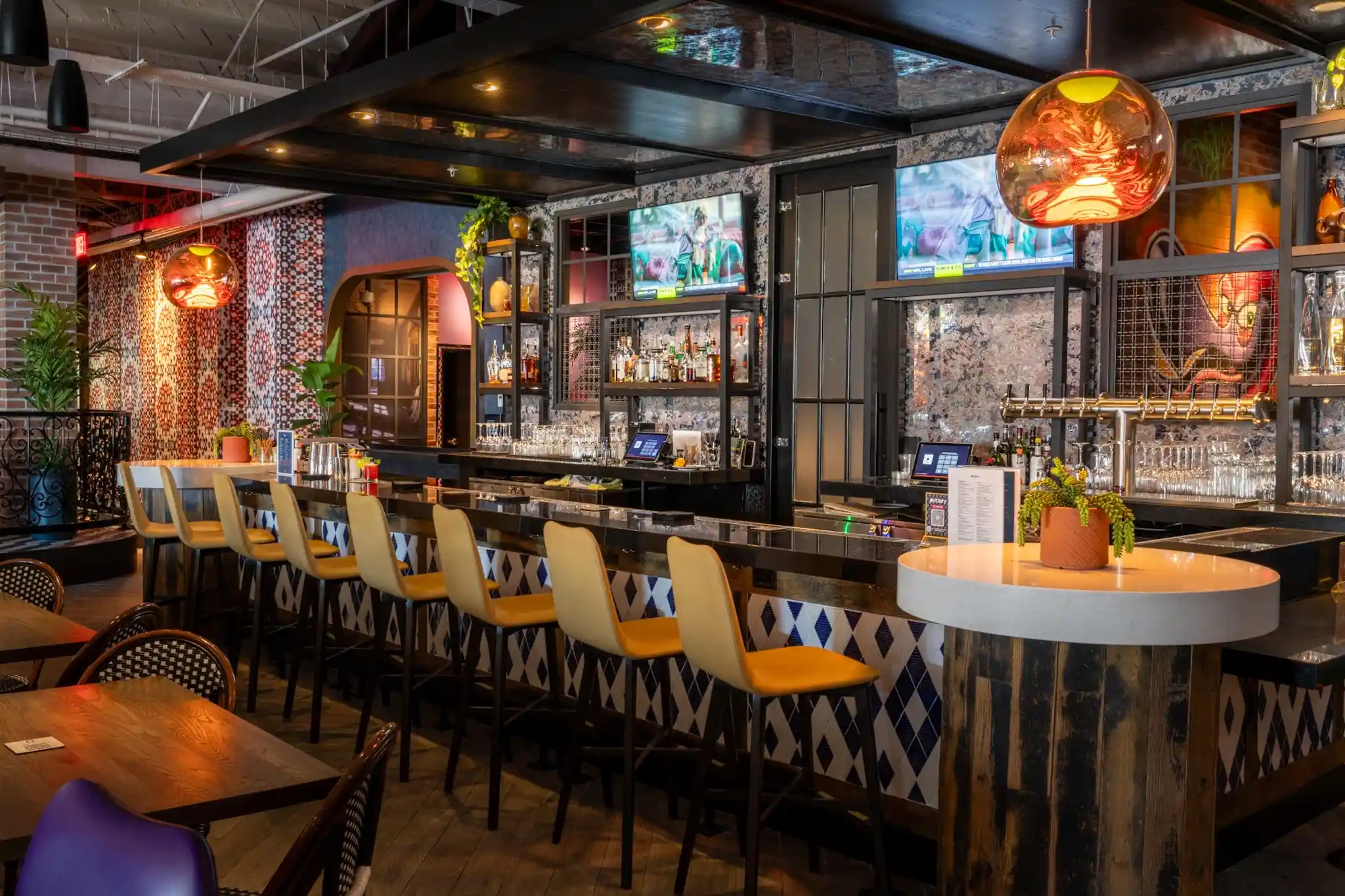 Main bar at Puttery Miami with yellow bar stools, black counters, pendant lights and a fully stocked back bar.