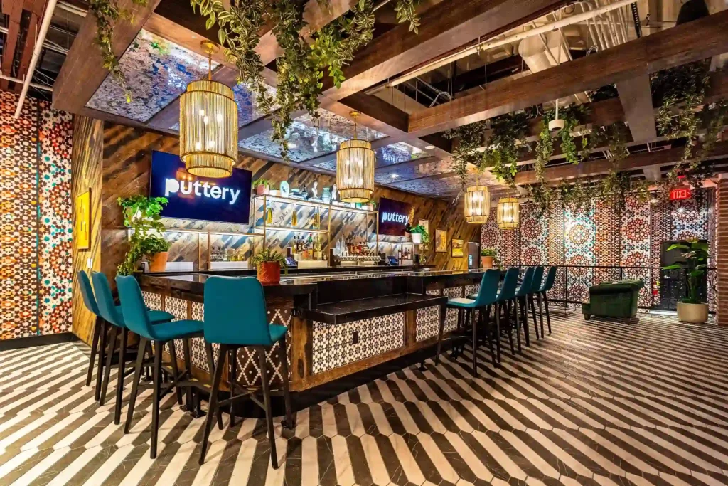 Upstairs bar at Puttery Miami with teal bar stools, hanging greenery, striped floors and patterned walls.