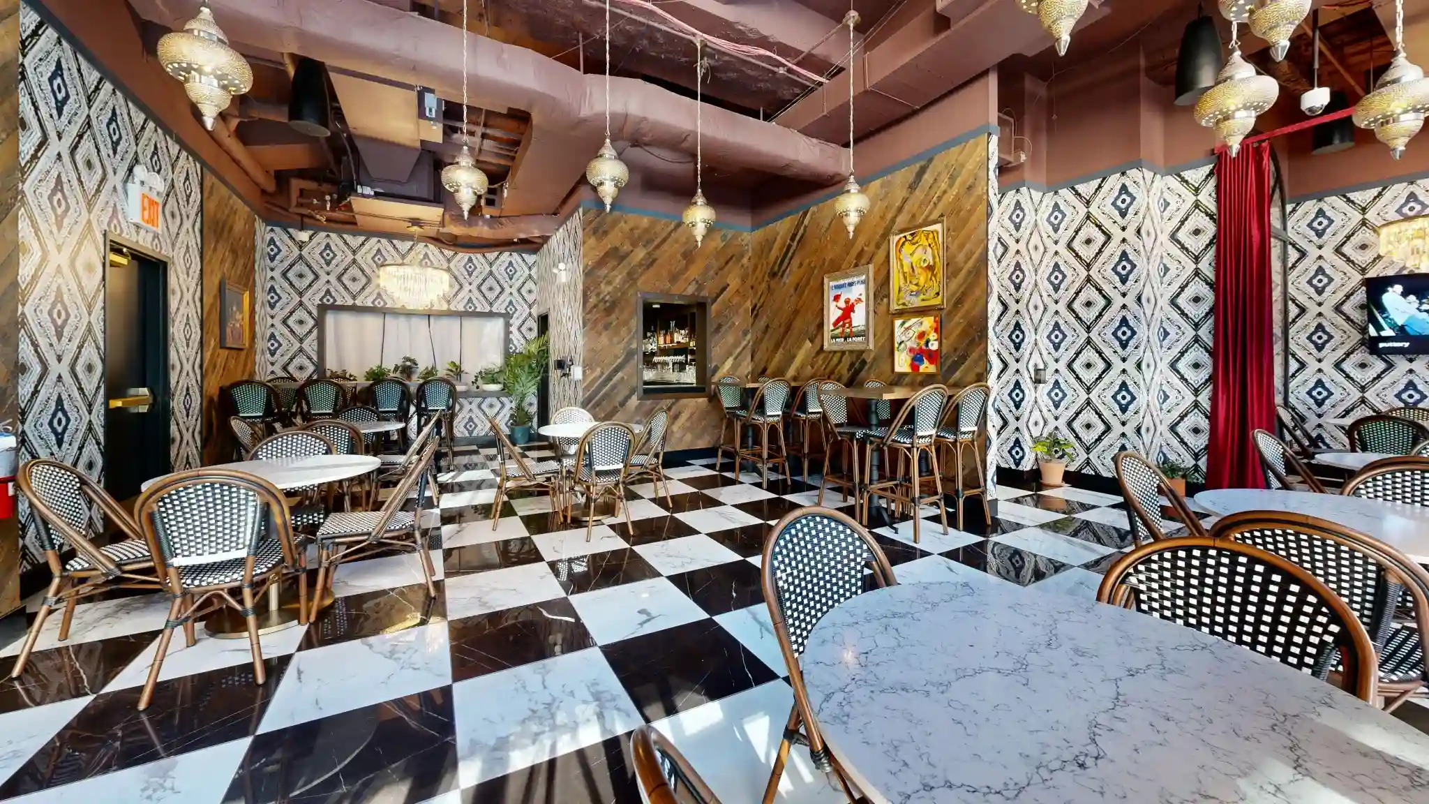Checkerboard dining room at Puttery New York City with marble tables, woven chairs, patterned walls and red curtains.