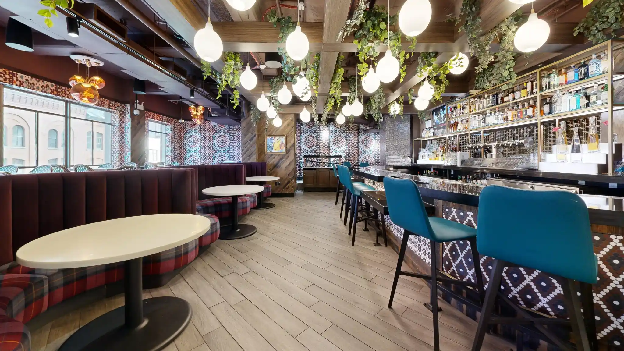 Main bar at Puttery New York City with teal bar stools, plaid banquettes, globe lights and hanging greenery.