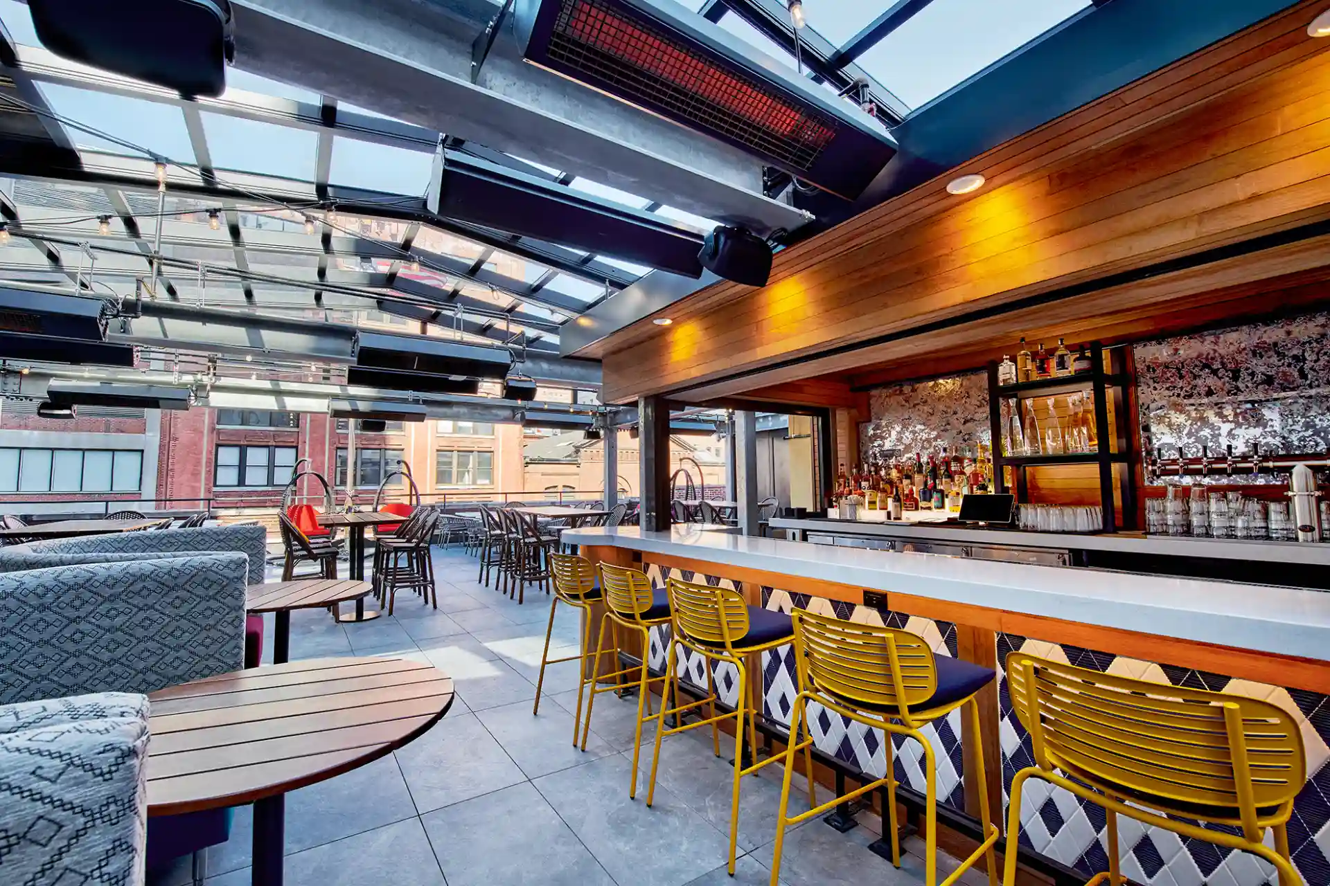 Rory’s Rooftop bar at Puttery New York City with yellow bar stools, a glass roof and city views.