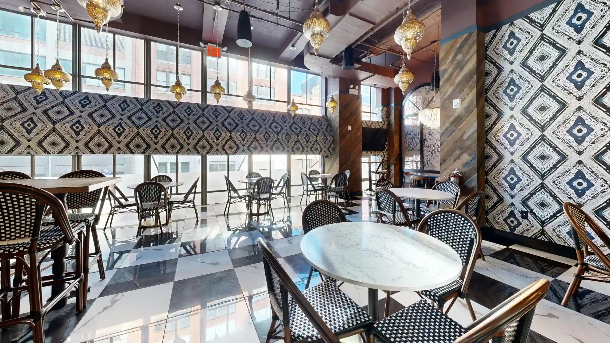 Window dining area at Puttery New York City with marble tables, woven chairs, patterned walls and pendant lights.