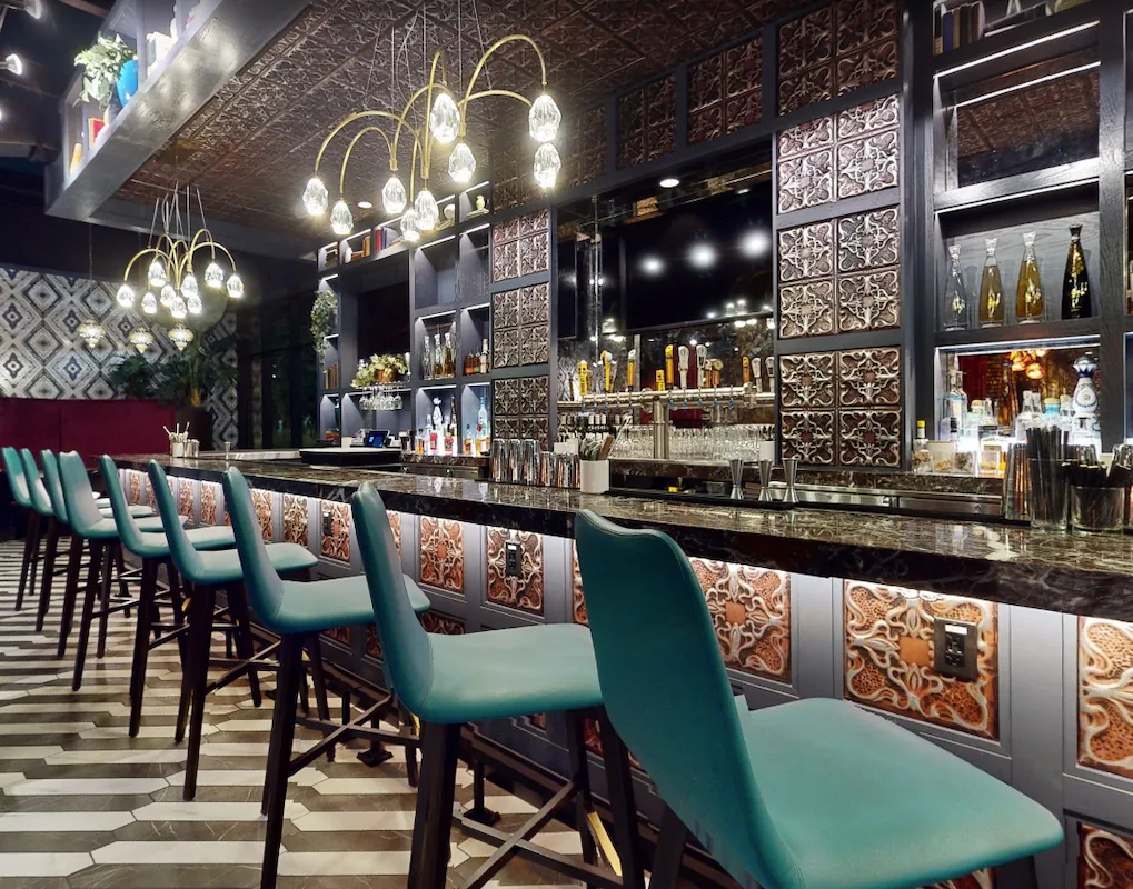 Main cocktail bar at Puttery Minneapolis with teal barstools, patterned tile and decorative lighting.