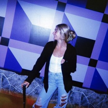 girl posing with putter in front of optical illusion mini golf course