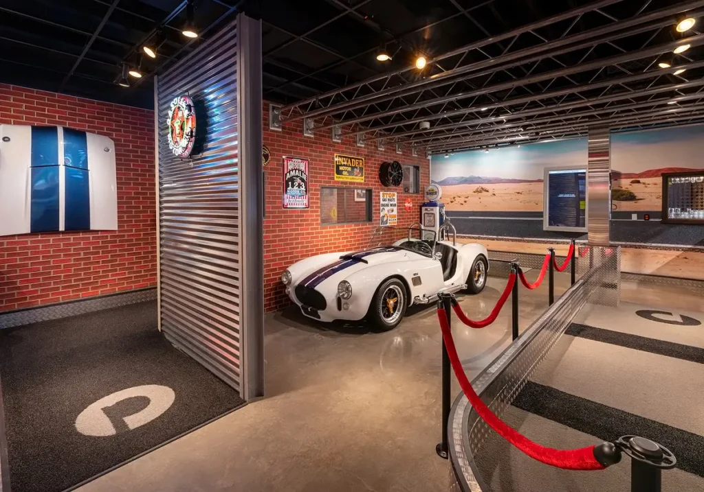 Roadster display area on the Garage Course at Puttery Pittsburgh with red rope barriers, desert mural and automotive-themed mini golf setting.