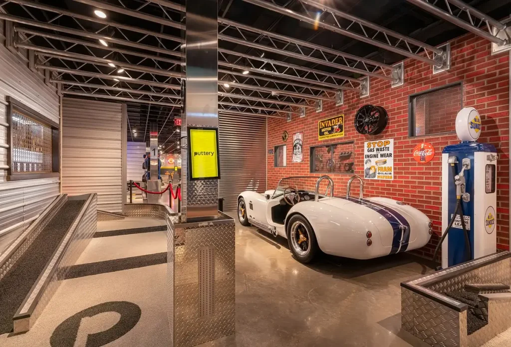 White roadster display on the Garage Course at Puttery Pittsburgh with vintage gas pump, brick walls and automotive-themed decor.