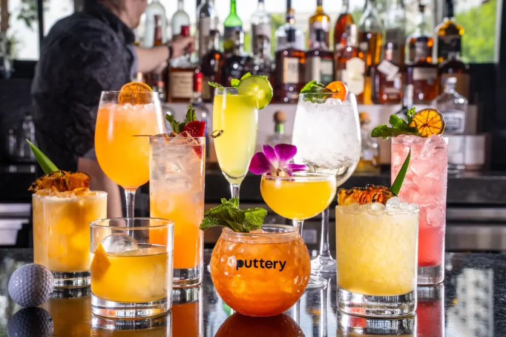 Assorted colorful cocktails displayed on the bar at Puttery with liquor bottles in the background.