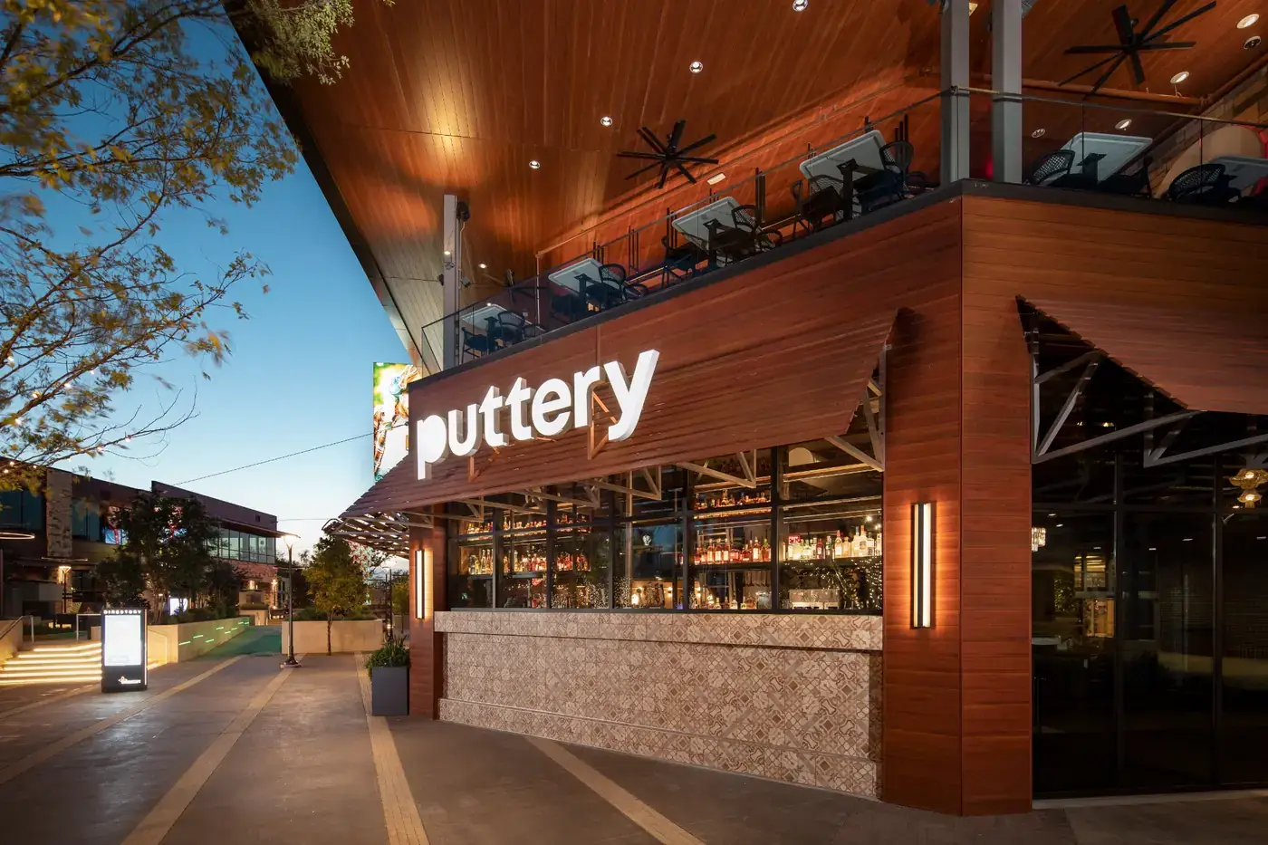 Exterior of Puttery Dallas at Grandscape, featuring the illuminated Puttery sign and modern two-story venue entrance at dusk.