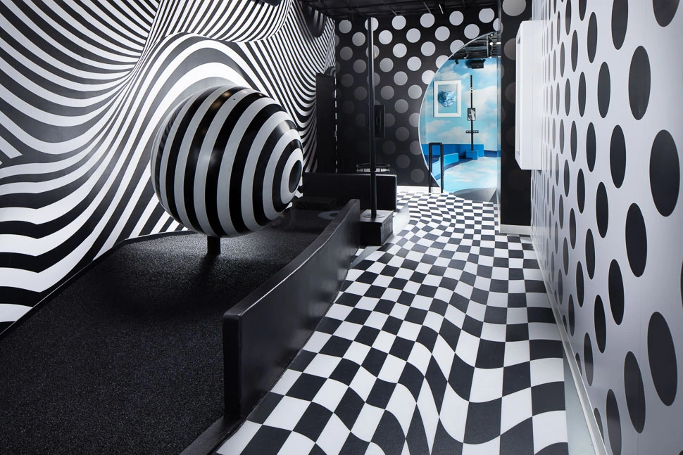 Black-and-white optical illusion indoor mini golf course at Puttery Dallas with warped patterns and a sculptural striped obstacle.
