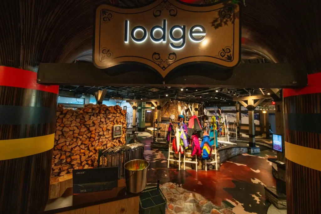 Entrance to the Lodge Course at Puttery Dallas in The Colony with ski jackets, stacked firewood and alpine mini golf decor.
