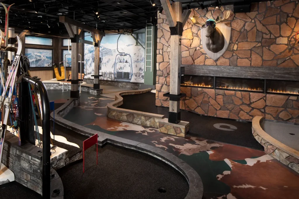 Lodge Course at Puttery Dallas in The Colony with a stone fireplace, mounted moose, ski equipment and mountain scenery.