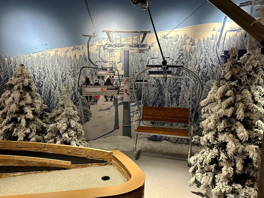 Ski lift scene on the Lodge Course at Puttery Dallas in The Colony with snowy trees, chairlift seating and mountain imagery.