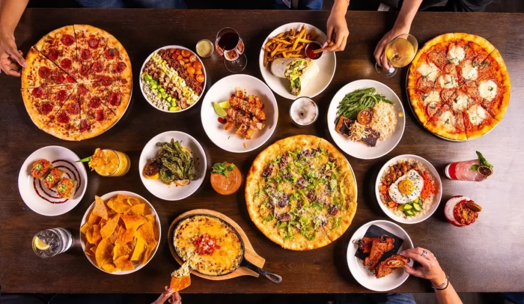 Top-down view of pizzas, shareables, bowls, wings, and cocktails spread across a table at Puttery.