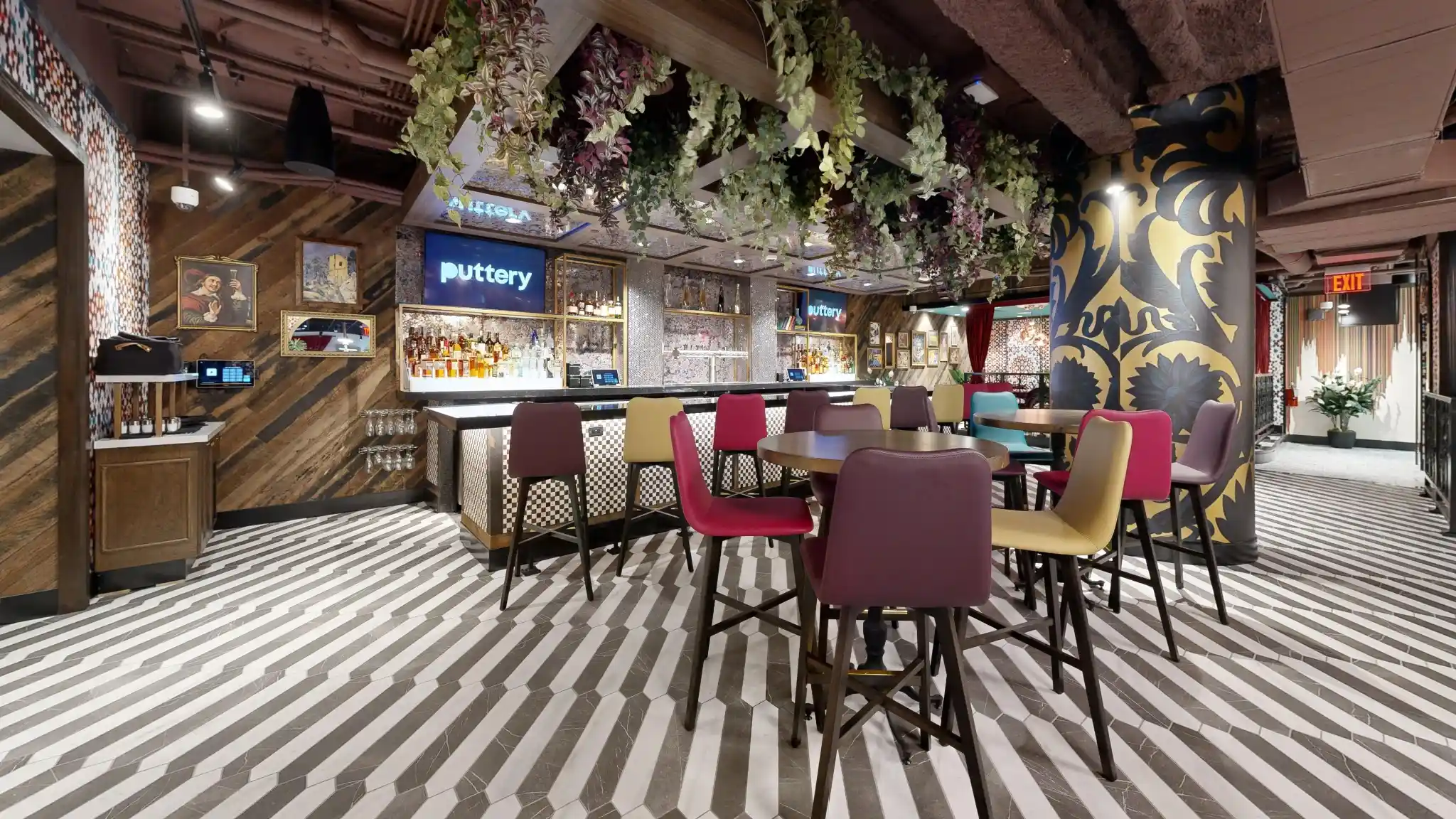 Craft cocktail bar at Puttery Kansas City with colorful seating, striped floors and hanging greenery.
