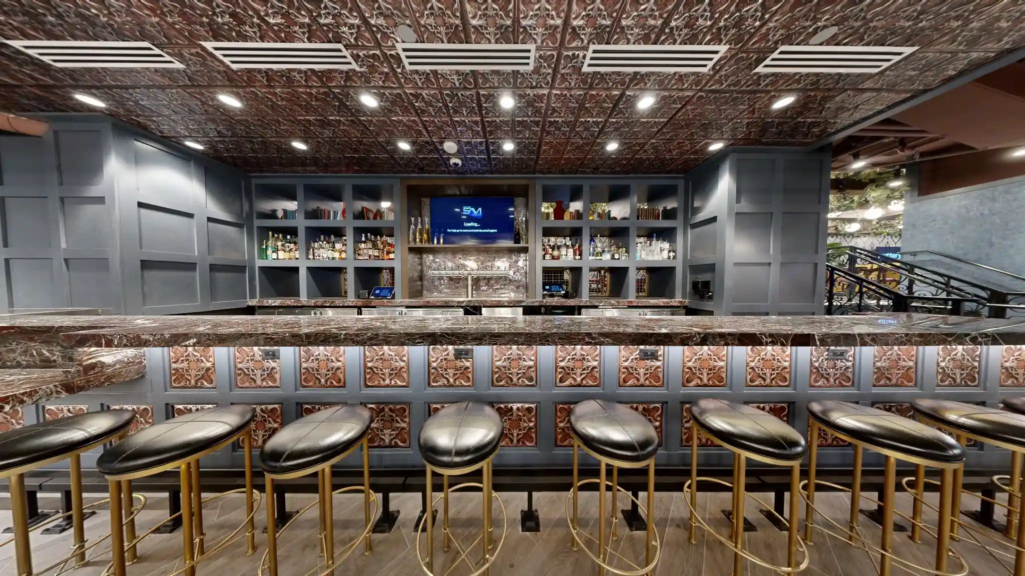 Main bar at Puttery Kansas City with marble counters, brass stools and an ornate metal ceiling.