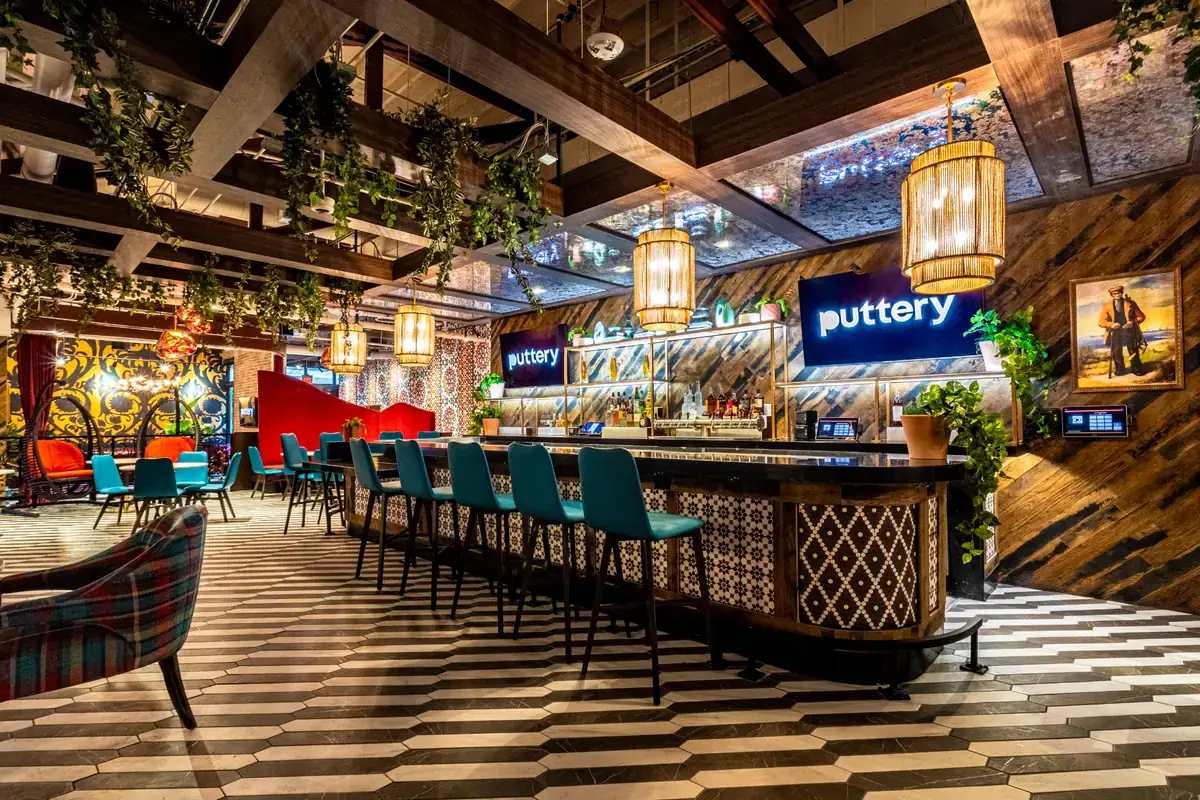 Interior bar at Puttery Miami with teal bar stools, hanging greenery, patterned floors, and illuminated Puttery signs.