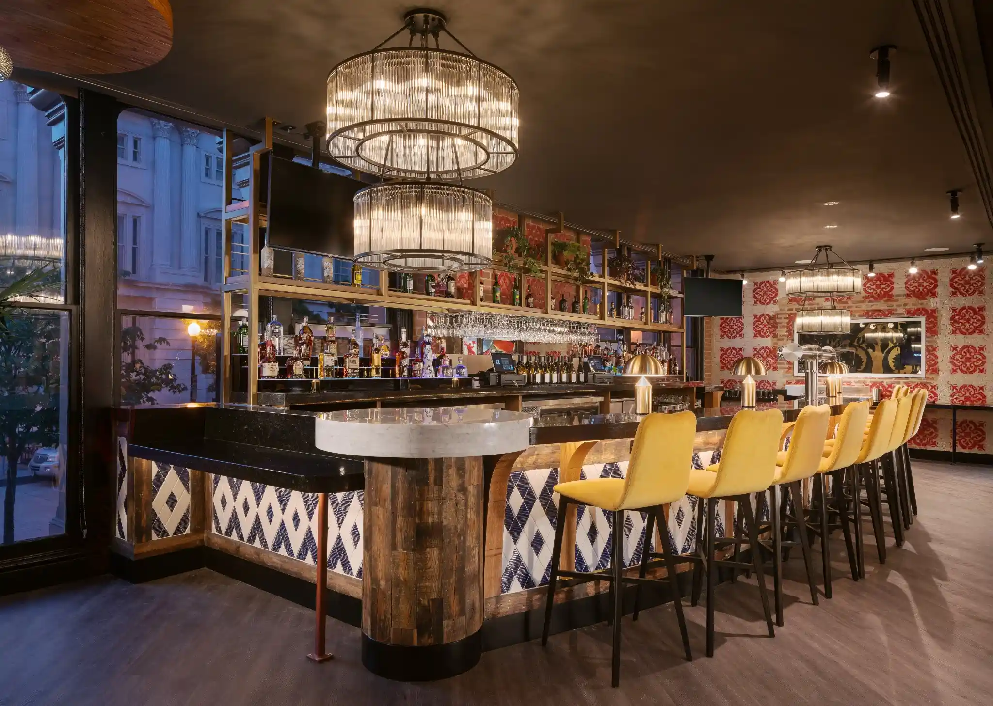 Main bar at Puttery Washington DC with yellow bar stools, chandeliers and back bar shelving.