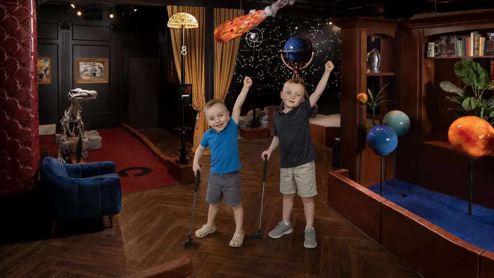 Two boys celebrate with mini golf putters inside an immersive course at Puttery Dallas.