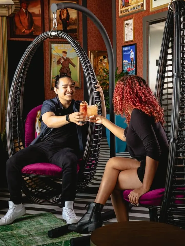 Two guests toasting craft cocktails in hanging lounge chairs at Puttery Dallas in Grandscape.