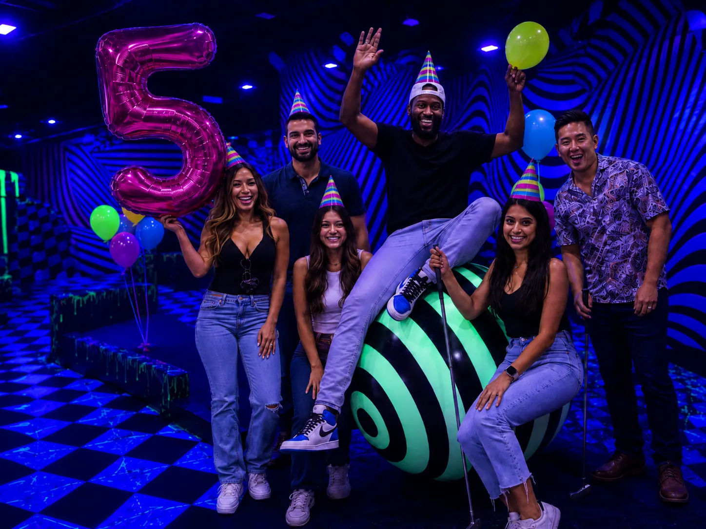 Group celebrating with a pink number 5 balloon inside Puttery Dallas’ Illusion Course, featuring updated glow-in-the-dark paint and bold blacklight stripes.