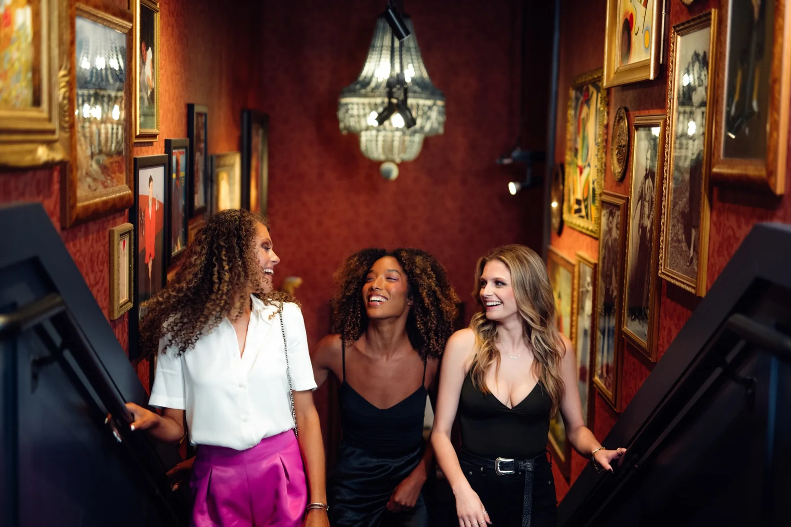 Three friends walking up a red stairwell lined with framed artwork inside Puttery.
