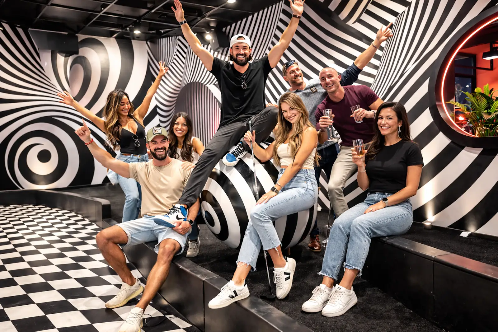 Group of guests posing and celebrating on a black-and-white illusion-themed mini golf course at Puttery.