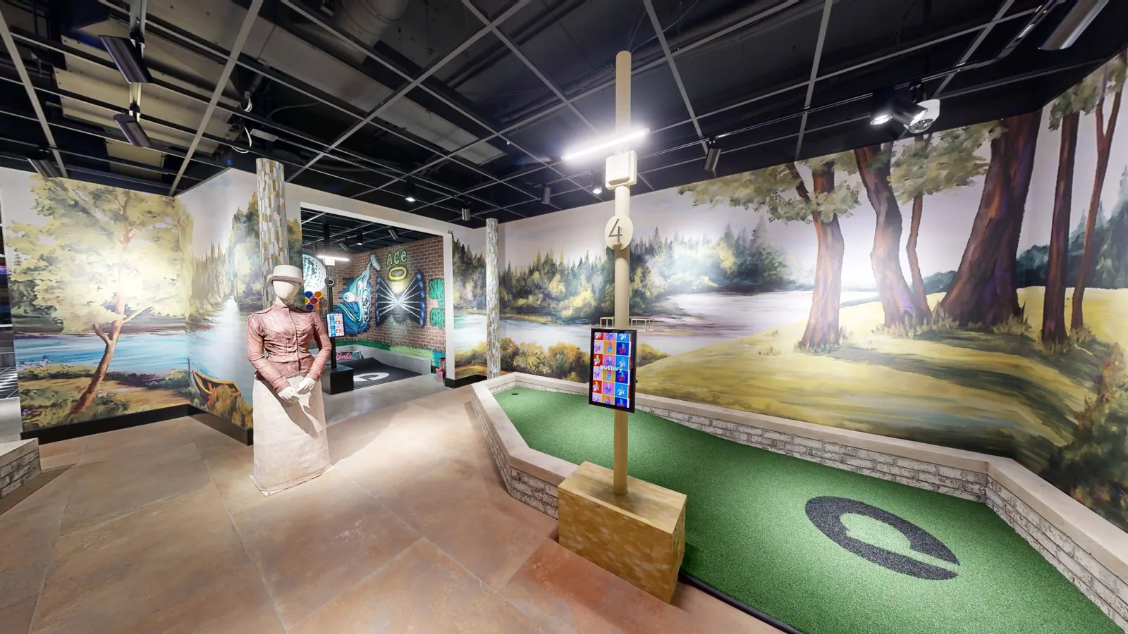 Landscape-inspired mini golf hole at Puttery Kansas City featuring mural walls, a mannequin figure and green putting turf.