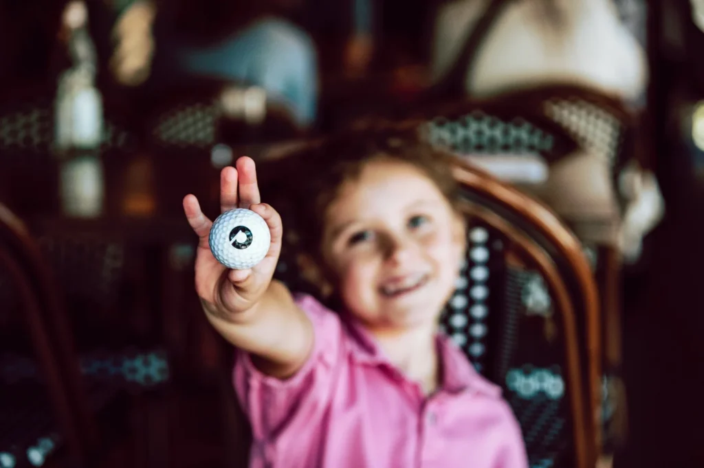 Child holding up a golf ball with the Puttery logo toward the camera.