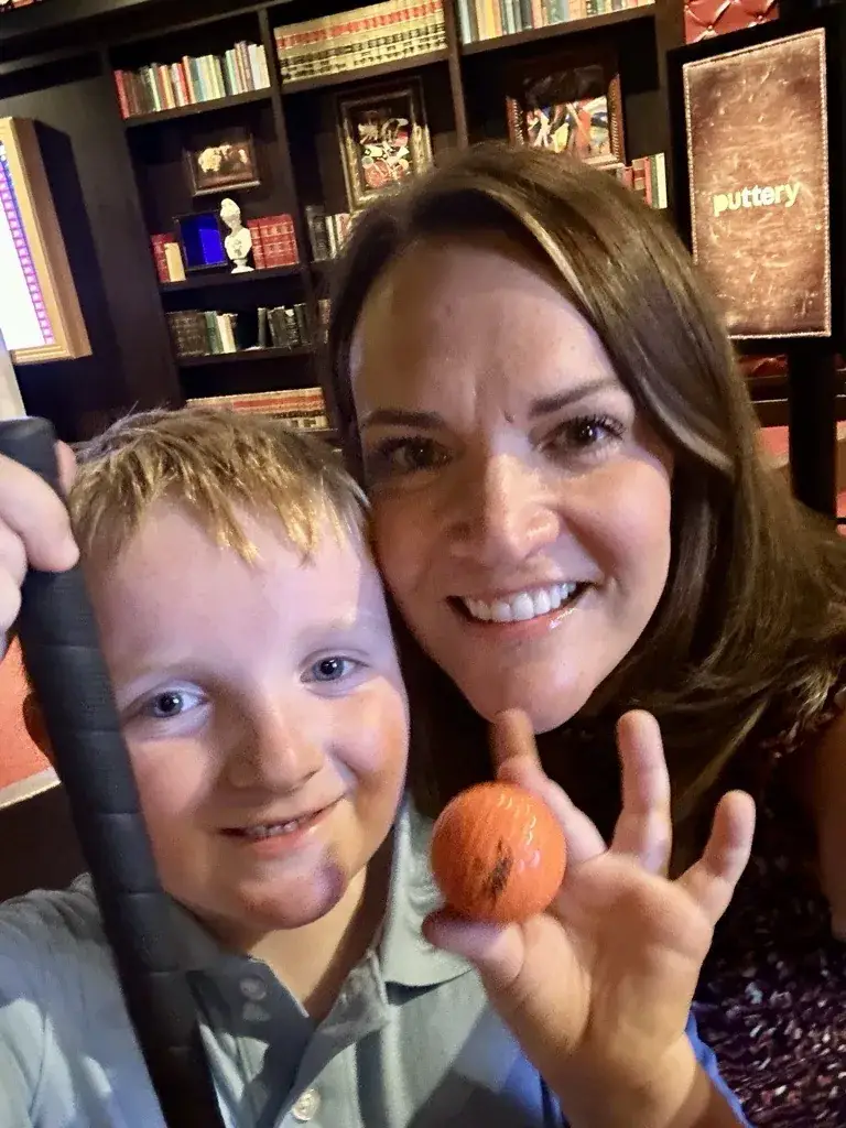 Mom and young son taking a selfie with an orange golf ball on the Library course at Puttery