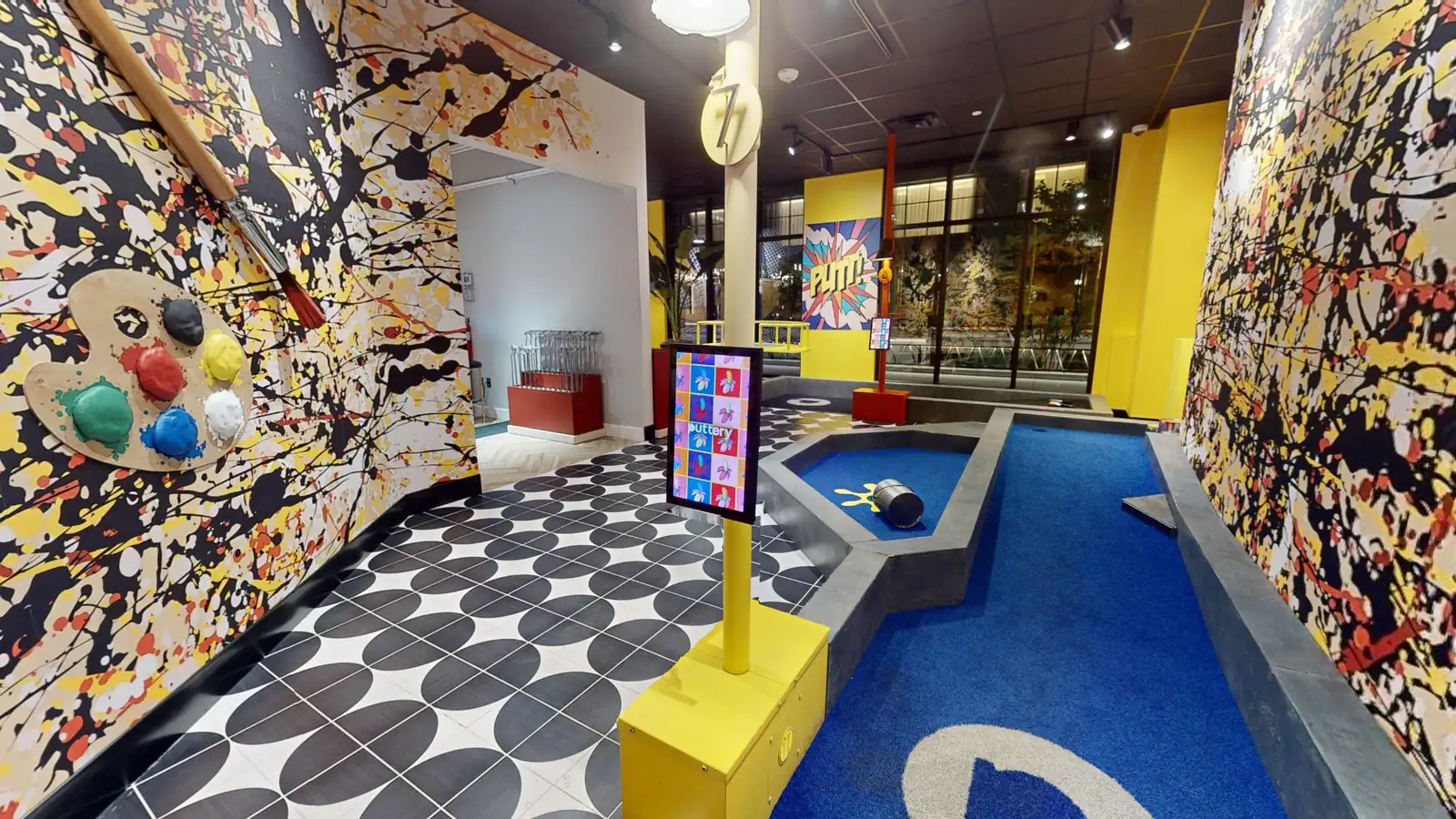 Pop art-themed indoor mini golf course at Puttery Minneapolis with colorful splatter-painted walls and blue putting greens.