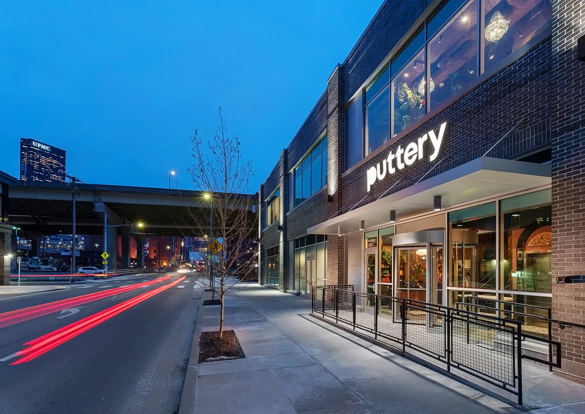 Exterior of Puttery Pittsburgh at dusk with illuminated signage, large windows and light trails along the street.