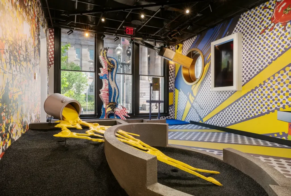 Pop art mini golf room with an oversized paintbrush and spilled yellow paint at Puttery Washington DC.