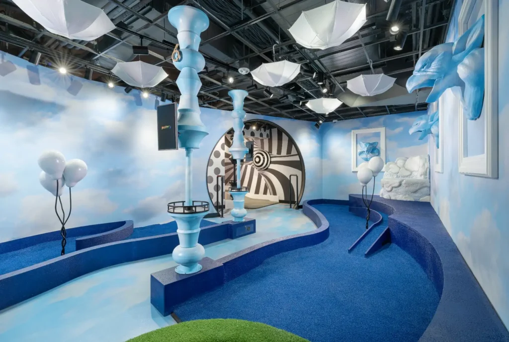 Blue mini golf room with cloud walls, upside-down umbrellas and oversized chess pieces at Puttery Washington DC.