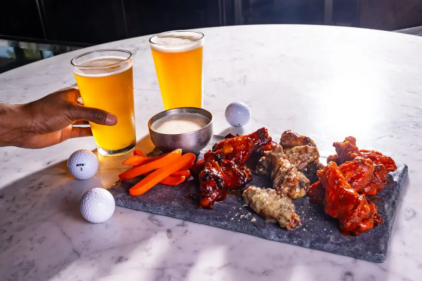 Wing Flight at Puttery with 12 bone-in wings served in three flavors—Kickin’ Bourbon, Truffle Honey Mustard and Garlic Parmesan—alongside carrot sticks, ranch and two cold pints of beer.