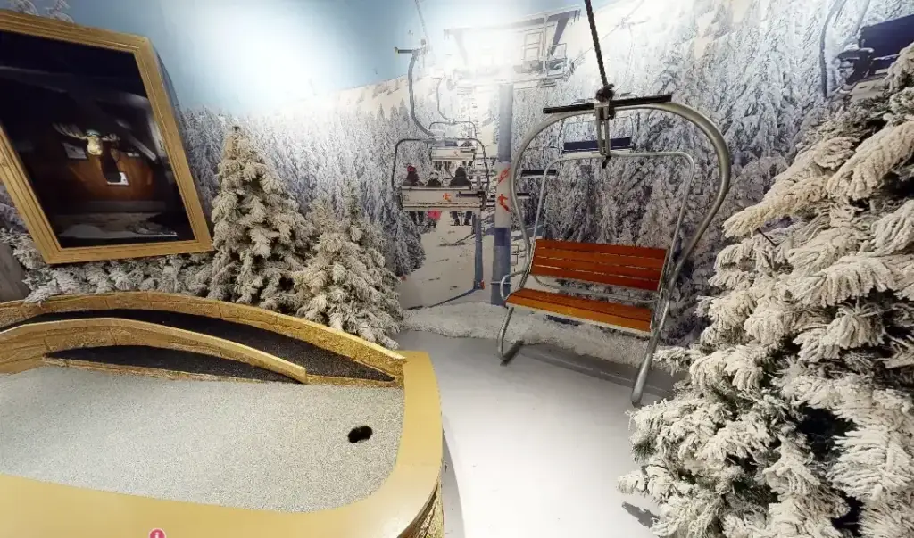 Snowy ski lift scene on the Lodge Course at Puttery Chicago with frosted trees, a chairlift seat and a winter mural backdrop.