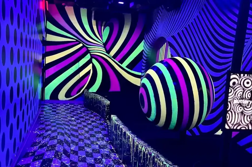 Glow-in-the-dark optical illusion mini golf hole with swirling neon patterns and a striped spherical feature inside the Illusion course at Puttery Dallas.