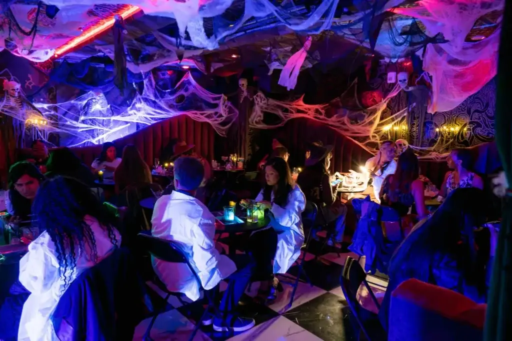 Frankenstein’s Cocktail Lab Crowd in Puttery NYC’s Rojo Room - Puttery Guests filling Puttery NYC’s Rojo Room during Frankenstein’s Cocktail Lab, surrounded by cobwebs, skeletons, candles and red-and-blue lighting.