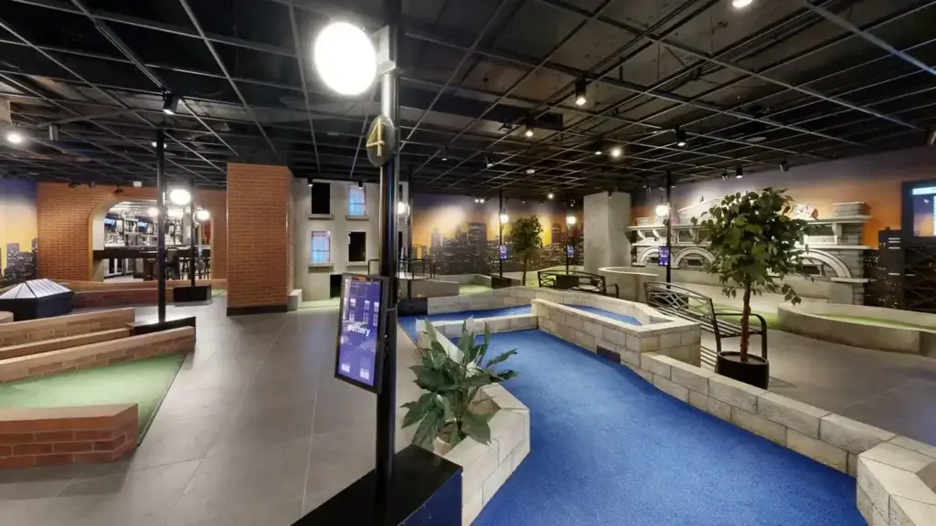 Wide view of the Rooftop mini golf course with blue turf, brick rooftop structures, and skyline murals at Puttery Kansas City.