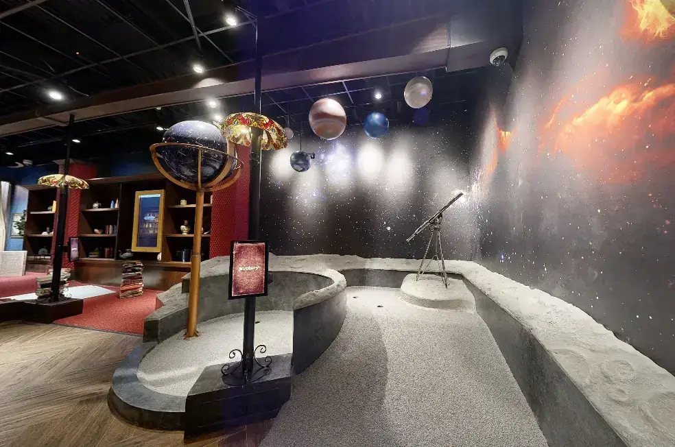 Space-themed hole on the Library Course at Puttery Miami with hanging planets, a telescope, star-filled walls, and an astronomy-inspired putting lane.
