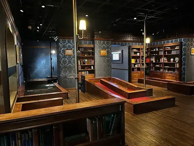 Library Course at Puttery Minneapolis with red putting lanes, dark wood bookshelves, patterned walls, and a constellation-themed section visible at the back of the course.