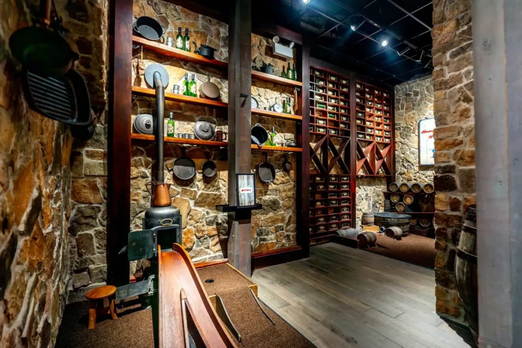 Rustic camp kitchen display with cookware, green bottles, stone walls, barrels, and shelving on the Lodge Course at Puttery New York City.
