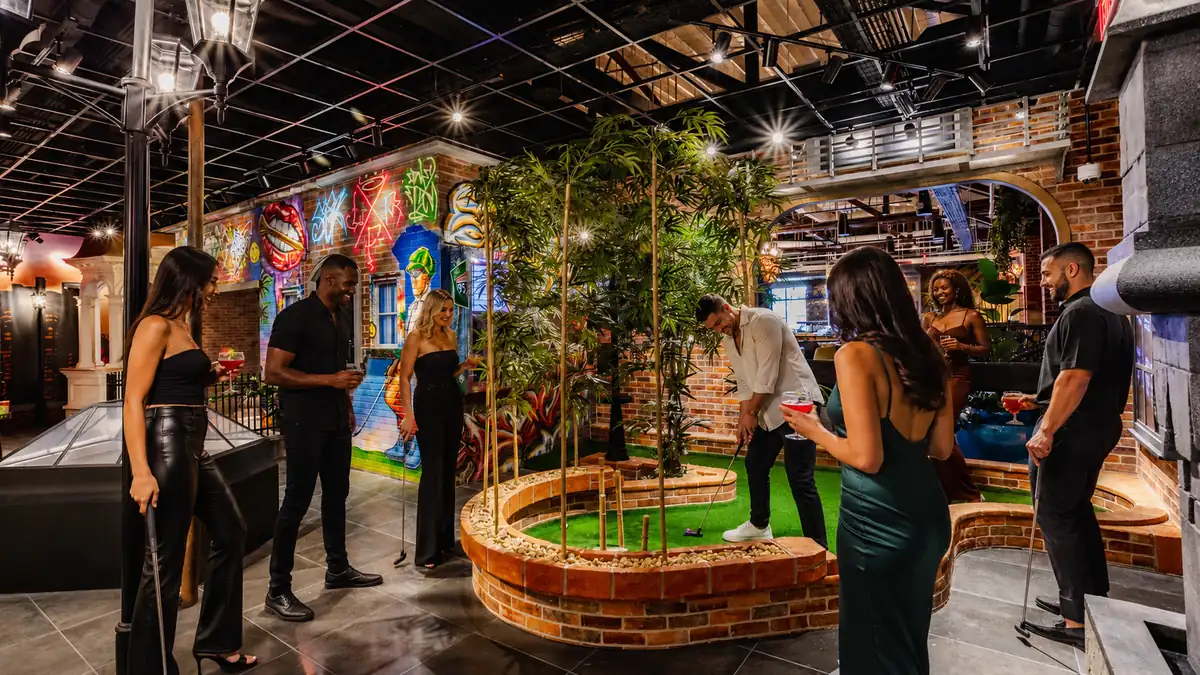 Adults playing indoor mini golf with cocktails during a birthday night out at Puttery Miami.