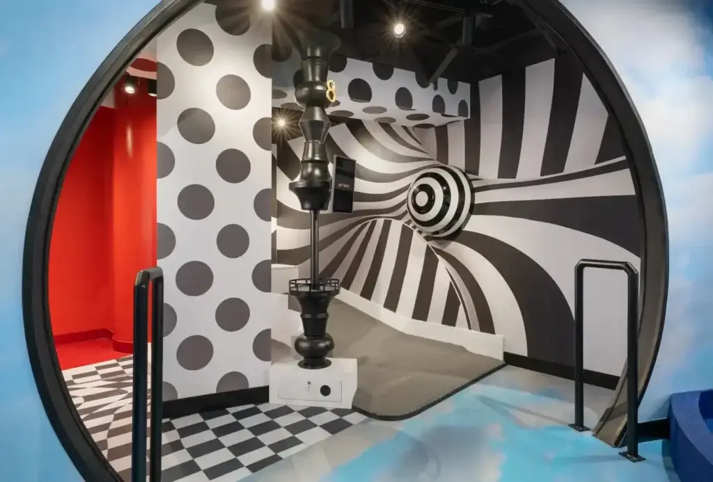 Entry view into a black-and-white illusion mini golf room with striped walls, polka dots, and a sculptural target feature at the Washington DC Illusion course.